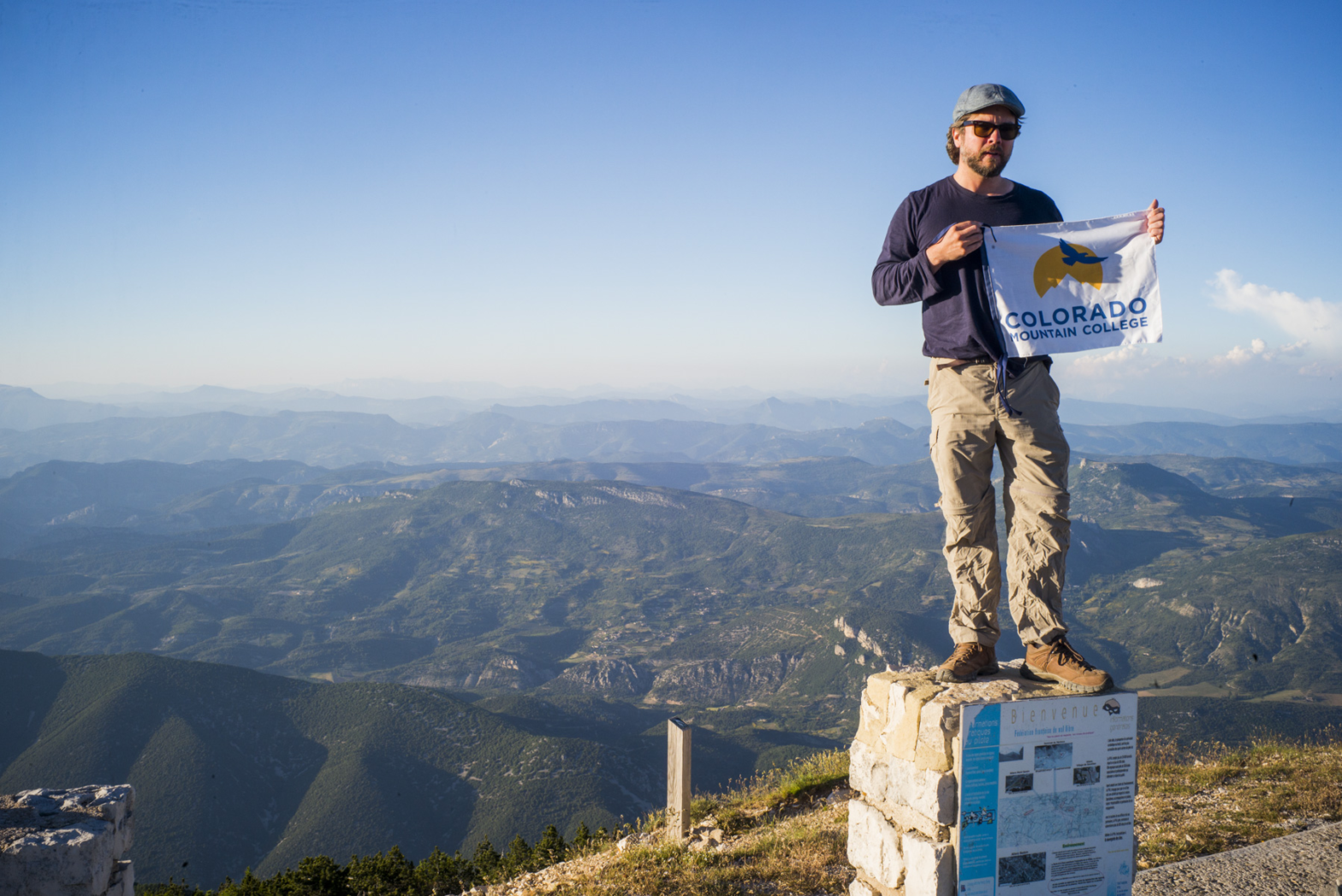 Photo of CMC photography faculty Joseph Gamble atop Mt Ventoux in France with a CMC Adventure Flag