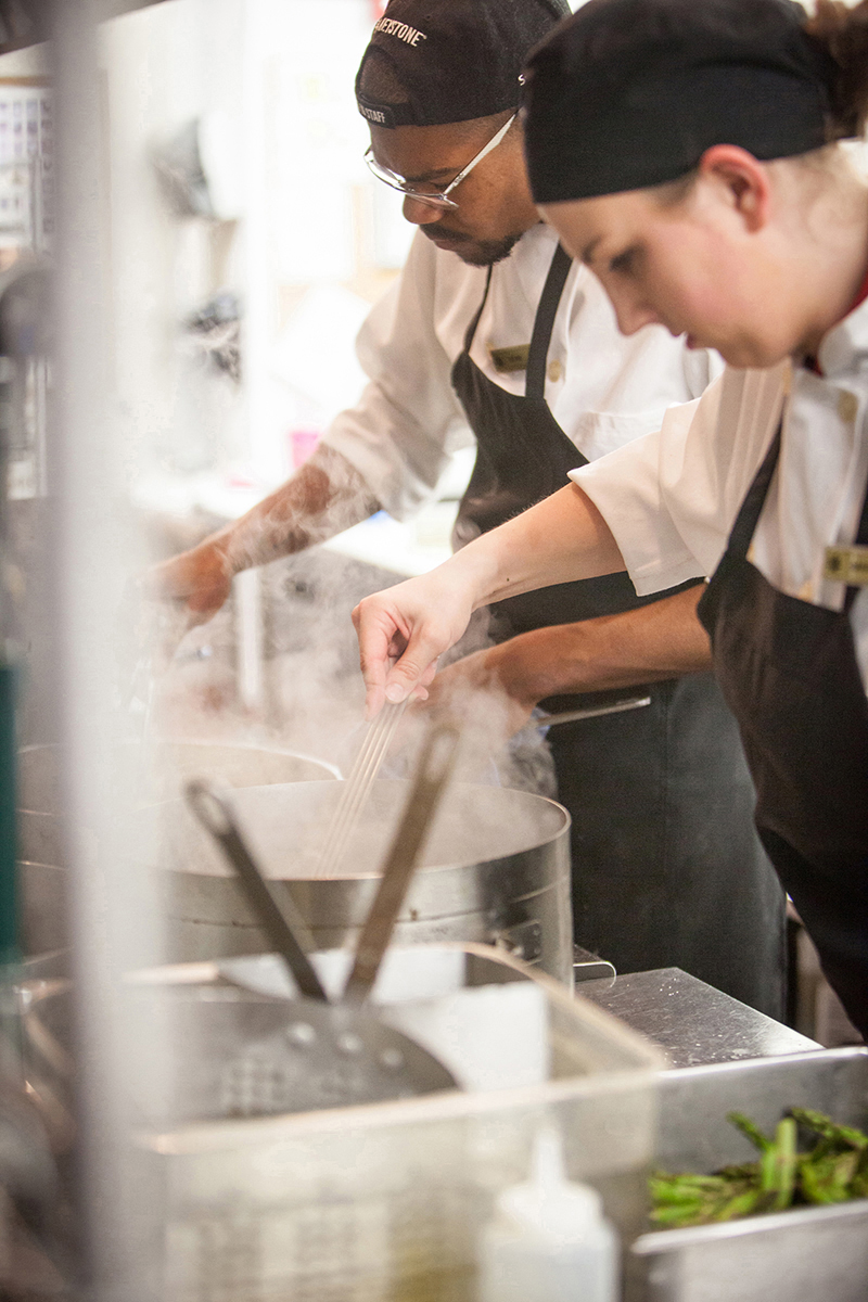 Chefs stir pots over stove.